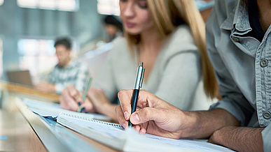 Studierende sitzen in einem modernen Hörsaal und machen Notizen in ihre Hefte. 